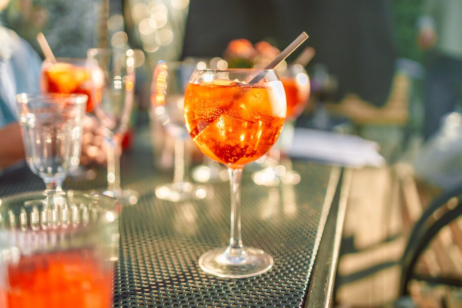 Aperol Spritz mit Strohhalm auf Tisch mit mehreren Gläsern | © Envato Elements