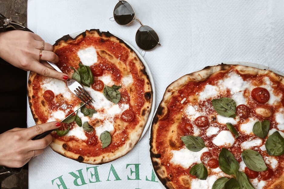 Hände einer Frau mit Besteck schneiden eine Pizza Margarita | © Pexels