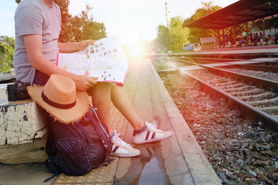 Tourist sitzt mit Rucksack und Sonnenhut auf Bank am Bahnhof | © Pexels