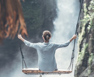 Urlauberin sitzt auf Holzschaukel vor Wasserfall | © Pexels