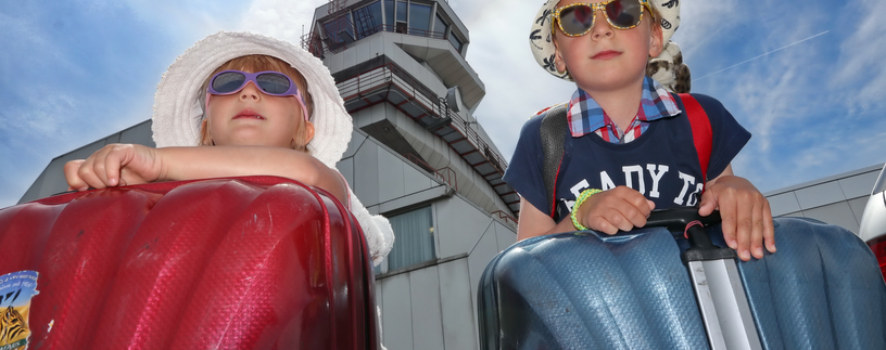 Geschwisterpaar mit Koffer, Sonnenbrille und Hut vor Tower | © Linz Airport