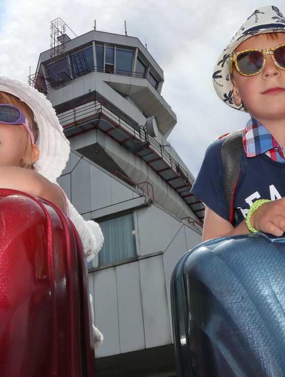 Geschwisterpaar mit Koffer, Sonnenbrille und Hut vor Tower | © Linz Airport