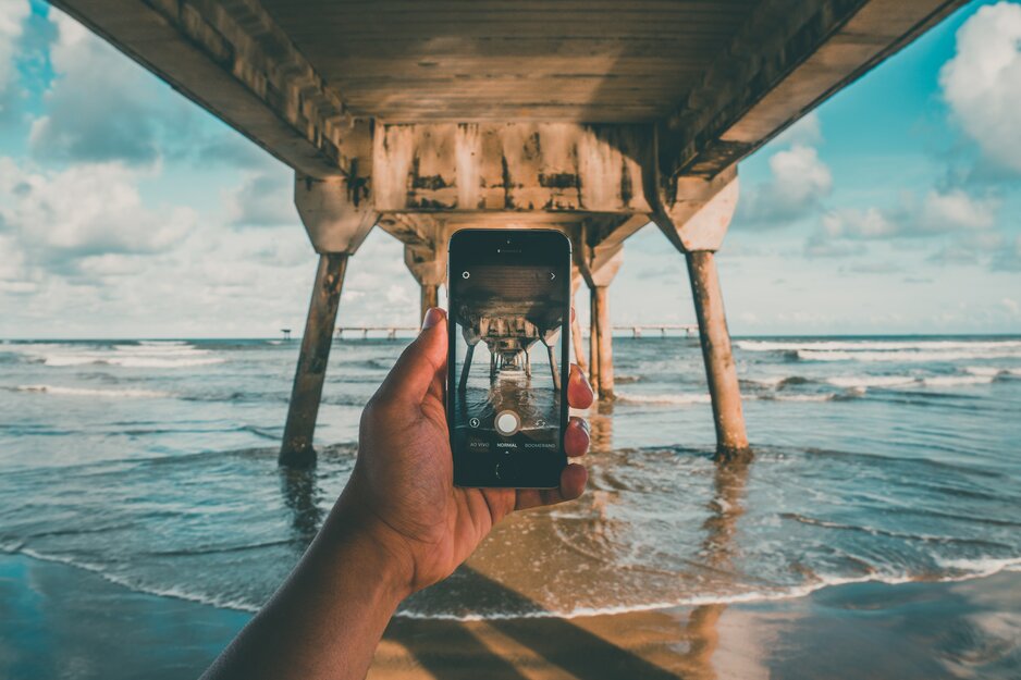 Handy beim Fotografieren unter einem Holzsteg in azurblauem Meer | © Pexels