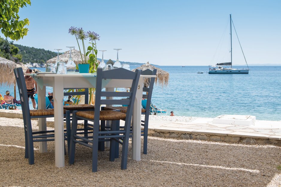 Tischchen mit Sessel am Alonissos Leftos Gialos Strand im Hintergrund ein Segelboot | © Springer Reisen