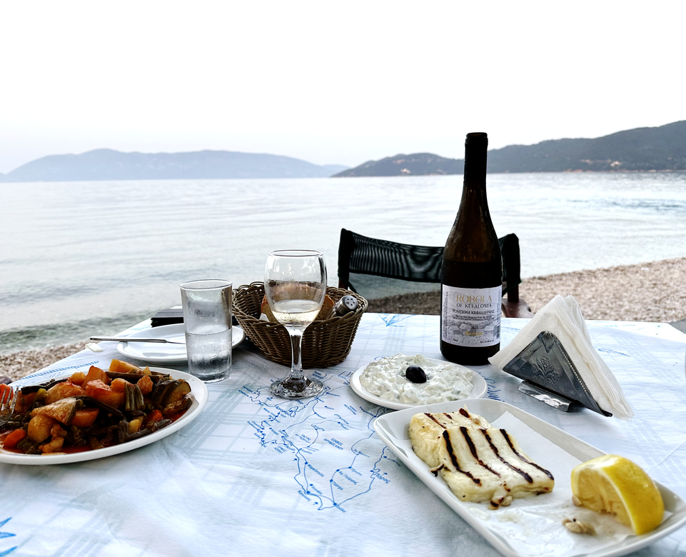 Tisch am Strand von Kefalonia gedeckt mit Tzatziki, gegrillten Käse und Gemüse und Wein | © Linz Airport