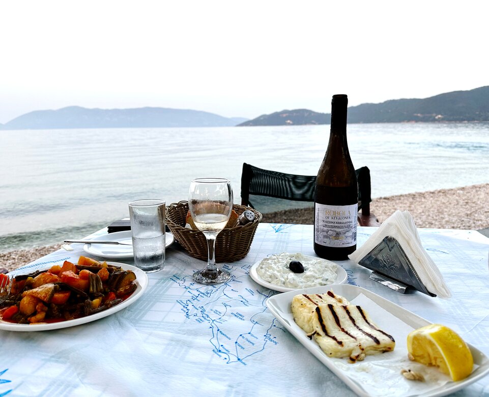 Tisch am Strand von Kefalonia gedeckt mit Tzatziki, gegrillten Käse und Gemüse und Wein | © Linz Airport