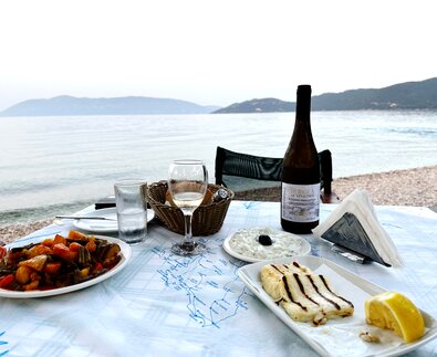 Tisch am Strand von Kefalonia gedeckt mit Tzatziki, gegrillten Käse und Gemüse und Wein | © Linz Airport