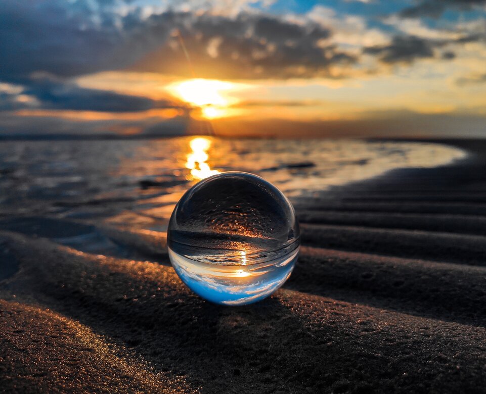 Glaskugel am Strand in der sich der Sonnenuntergang spiegelt | © unsplash