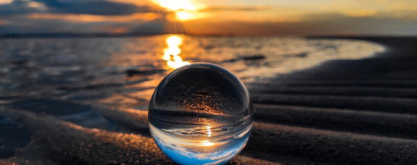 Glaskugel am Strand in der sich der Sonnenuntergang spiegelt | © unsplash