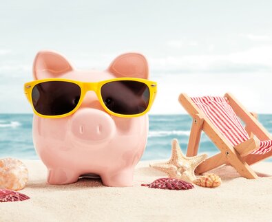 Pinkes Sparschwein mit gelber Sonnenbrille am Strand | © Adobe Stock