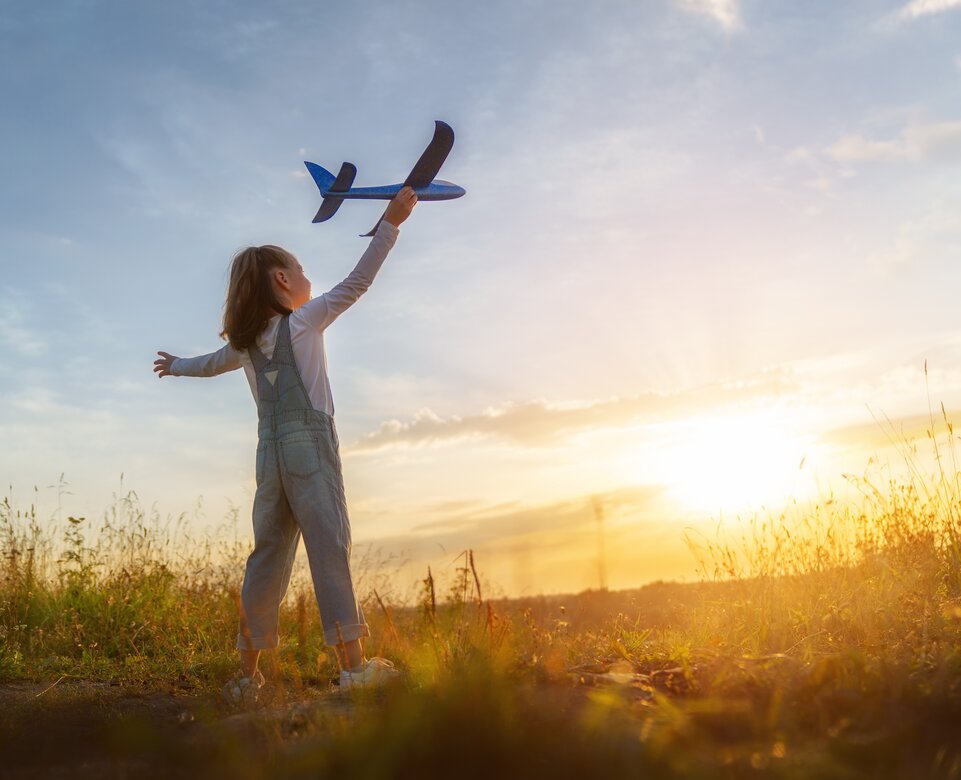 Kleines Mädchen mit Spielzeugflugzeug in der Hand im Sonnenschein auf Wiese | © Envato Elements