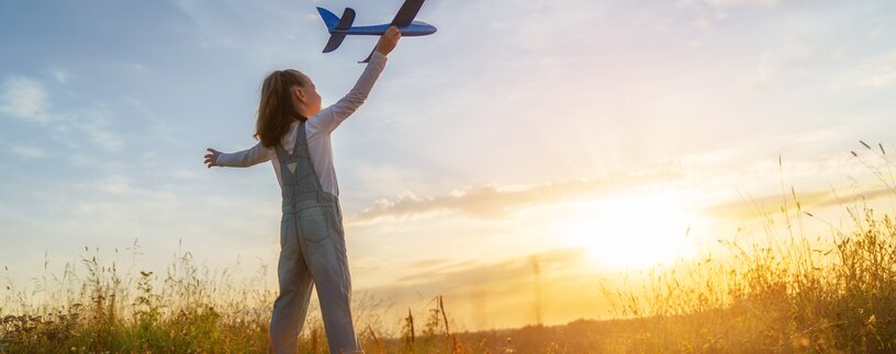 Kleines Mädchen mit Spielzeugflugzeug in der Hand im Sonnenschein auf Wiese | © Envato Elements