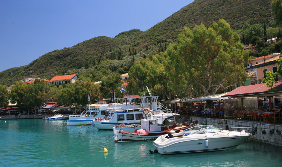 Boote ankern im Hafen entlang einer Promenade mit Restaurants, im Hintergrund grünbewaldete Hügel | © Rhomberg Reisen